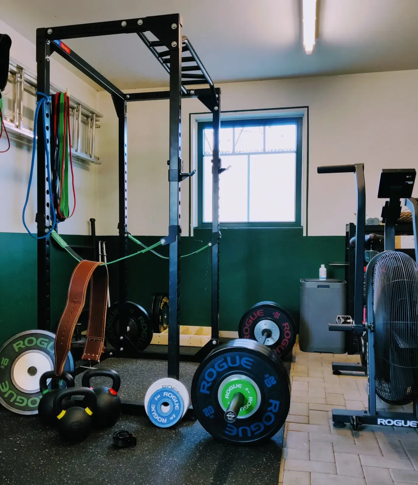 a home gym with a rack, barbell, weights, bands, kettlebells, and an Echo Bike