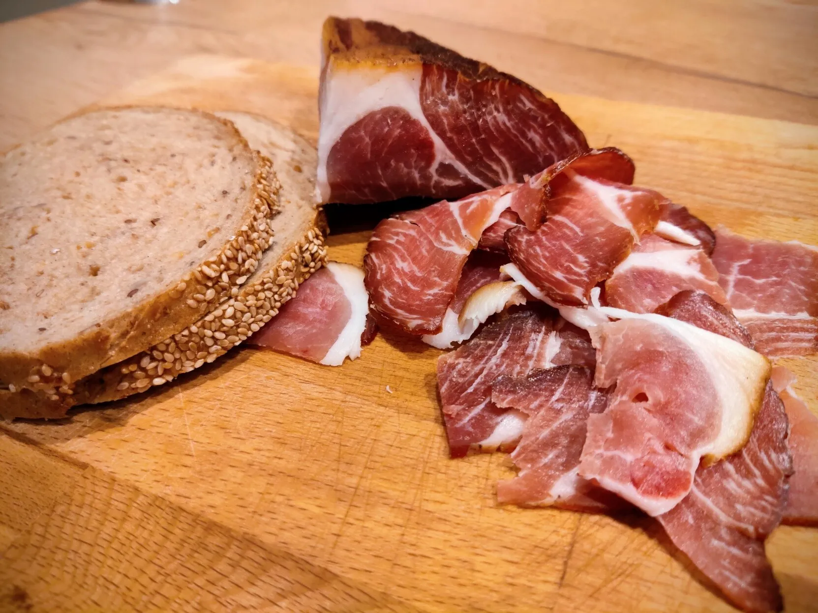Slices of ham on a wooden board with two slices of bread on the side