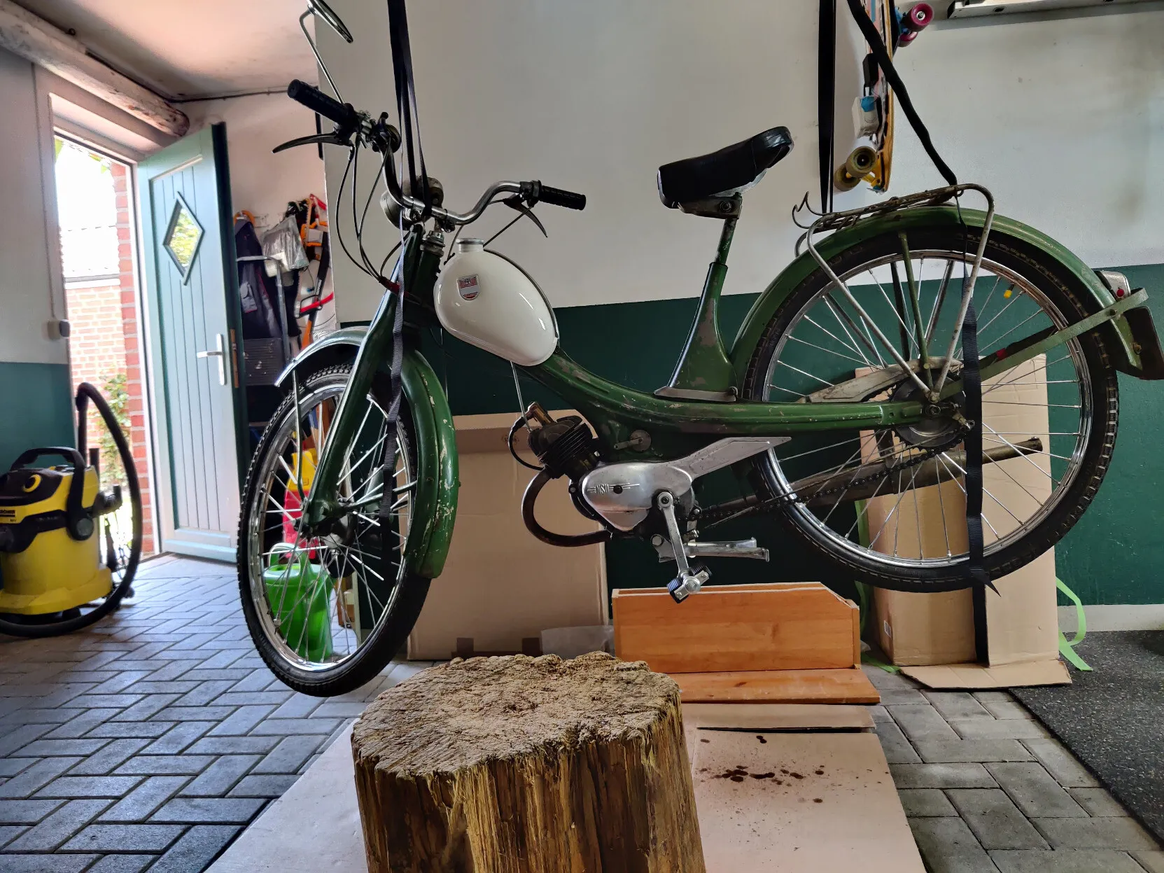 A green and white NSU Quickly moped hanging from a garage ceiling