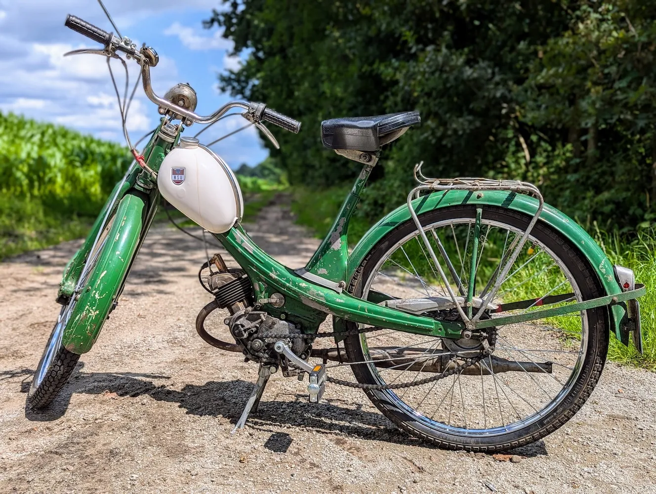A green NSU Quickly moped standing on a gravel path next to a corn field