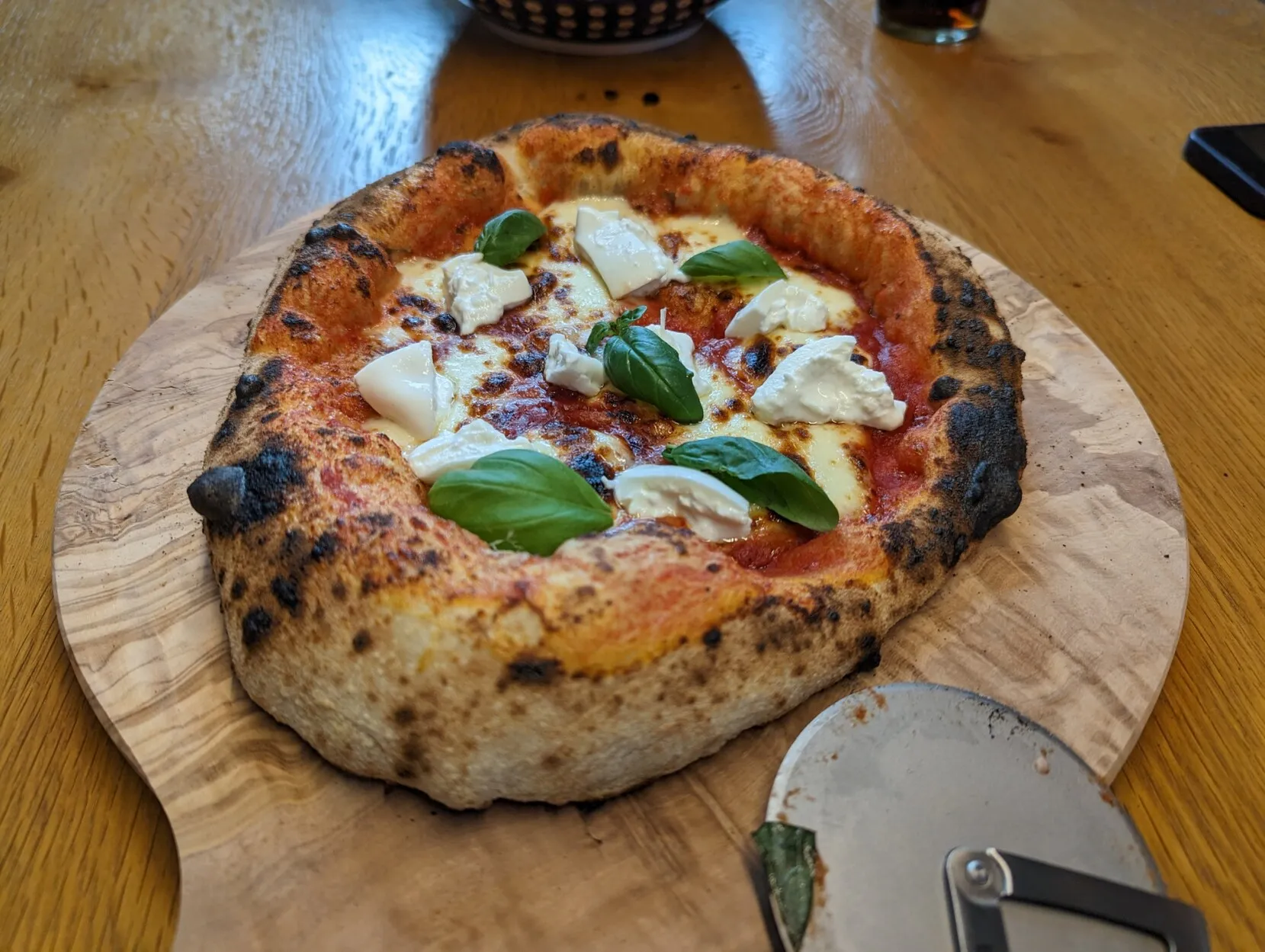 A Neapolitan style pizza sitting on a wooden board. The pizza is topped with burrata and decorated with fresh basil.